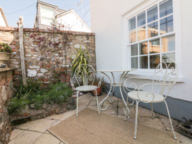 An outdoor patio area with two metal chairs and a round table near a window and stone wall at Searles in Lympstone