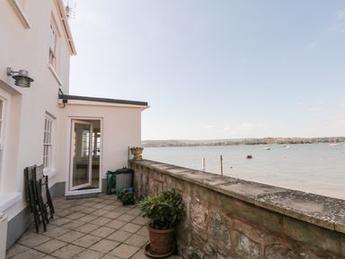 A patio with tiled floor and plants overlooking a body of water at Searles in Lympstone