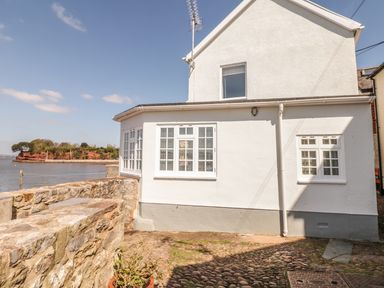 The exterior of a white house with multiple windows near a stone wall and water at Searles in Lympstone