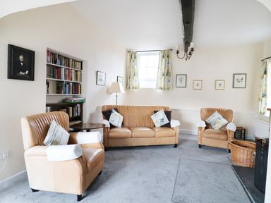 A sitting room with beige leather sofas armchairs a bookshelf and a window at Glebe House in Wells