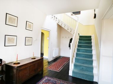 A hallway with a green carpeted staircase wooden chest of drawers and framed pictures on the wall at Glebe House in Wells