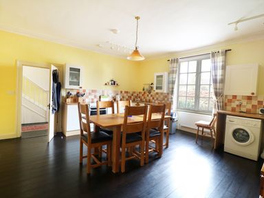 A kitchen with wooden dining table and chairs window with checkered curtains washing machine and yellow walls at Glebe House in Wells