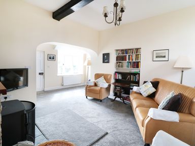 A living room with beige chairs a sofa bookshelf and a TV at Glebe House Wells