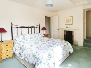 A bedroom with a bed floral bedspread two wooden nightstands lamps fireplace and framed picture at Glebe House in Wells