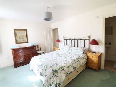 A bedroom with a bed with floral bedding two wooden bedside tables with red lamps a wooden dresser with a mirror and a wooden chair at Glebe House in Wells