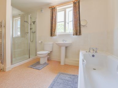 A bathroom with a shower enclosure toilet pedestal sink bathtub and window with curtains at Glebe House in Wells