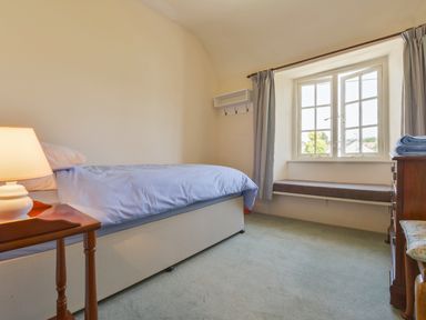 A bedroom with a bed, bedside table with lamp, window seat under a window with curtains and a wooden dresser at Glebe House in Wells