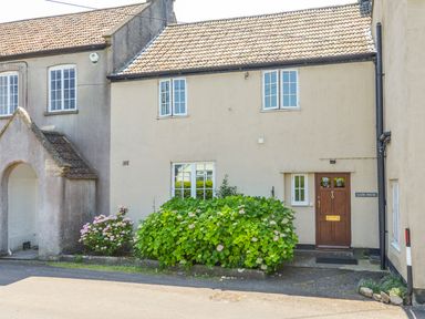 The exterior of a beige house with a tiled roof and brown door with plants in front at Glebe House in Wells
