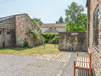 An outdoor area with a wooden bench gravel driveway stone walls and a metal gate at Glebe House in Wells