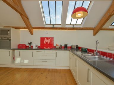A kitchen with white cabinets black countertops red backsplash and skylights at Old Armoury Barn in Ashburton