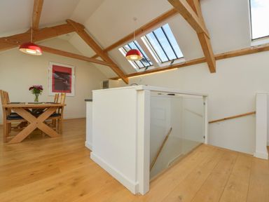 A dining area with wooden table and chairs flowers on the table skylights and exposed wooden beams at Old Armoury Barn in Ashburton
