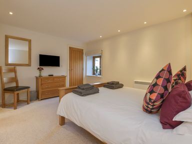 A bedroom with a bed folded towels wooden chair wooden dresser mirror and small window at Old Armoury Barn in Ashburton