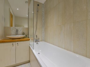 A bathroom with a bathtub and shower next to a wooden countertop with a vessel sink at Old Armoury Barn in Ashburton