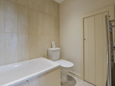A bathroom with a bathtub a toilet a tiled wall and a wooden door at Old Armoury Barn in Ashburton