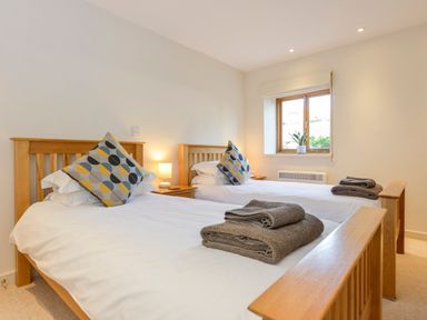 A bedroom with two wooden beds white bedding and patterned pillows at Old Armoury Barn in Ashburton