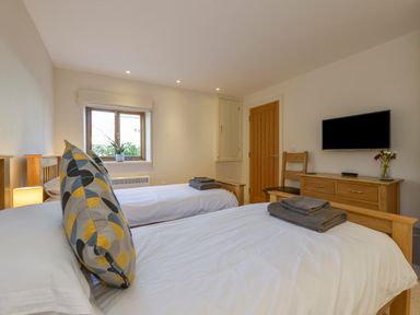 A bedroom with two beds tv on wall wooden dresser and chair at Old Armoury Barn in Ashburton
