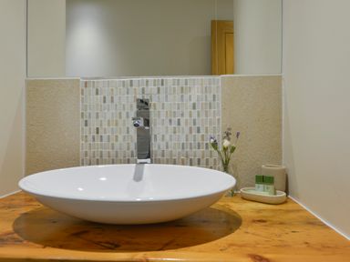 A bathroom sink with a modern faucet flowers and toiletries on a wooden countertop at Old Armoury Barn in Ashburton