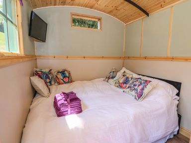 A bedroom with a bed and colorful dog-themed pillows and a stack of folded purple towels at Railway Carriage in Govilon