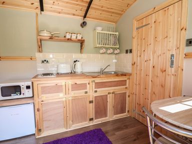 A small kitchen with wooden cabinets microwave toaster kettle and a dining table at Railway Carriage in Govilon