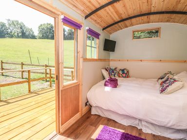 A bedroom with a bed and colorful pillows near a wooden deck outside at Railway Carriage in Govilon