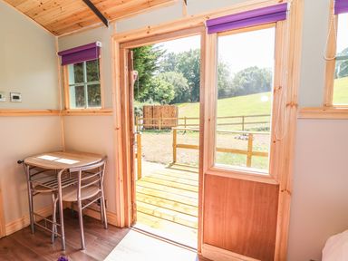 A small table with two chairs in a wooden room with an open door to a deck and grassy area at Railway Carriage in Govilon