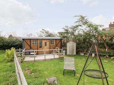 A fenced garden with a wooden shed patio chairs a metal fire pit and a small storage shed at Railway Carriage in Govilon