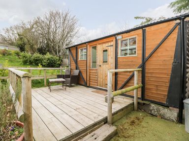 A wooden deck with two chairs and a small table outside a wooden building at Railway Carriage in Govilon