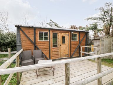 A wooden cabin with two wicker chairs and a table on a wooden deck at Railway Carriage in Govilon