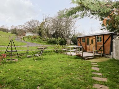 A grassy yard with a wooden cabin and a metal bench near a fire pit at Railway Carriage in Govilon