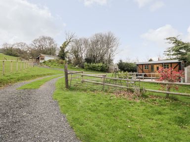 A gravel path with wooden fences leading to small buildings in a grassy area at Railway Carriage in Govilon