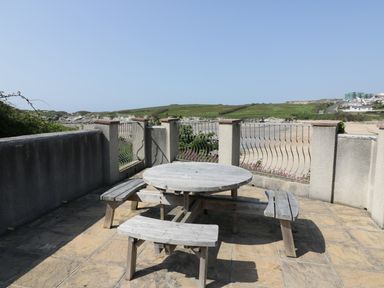 A circular wooden picnic table with benches on a stone patio overlooking a beach and green hills at Seashore House in Porth