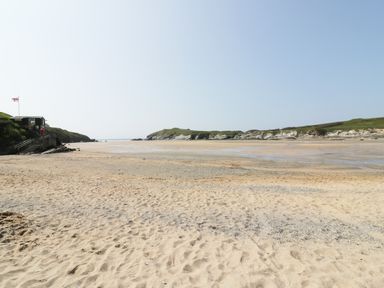 A sandy beach with a small building and flag on the left and rocky cliffs in the background at Seashore House in Porth