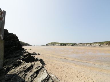 A sandy beach with rocky cliffs and grassy hills under a clear sky at Seashore House in Porth