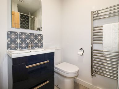 A bathroom with a sink vanity, toilet, towel rail with towel, and decorative tiles at Trenant View in Wadebridge