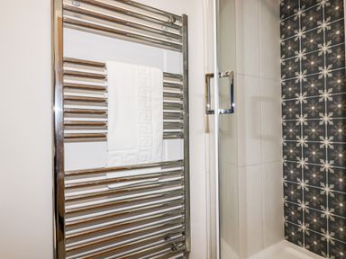 A bathroom with a chrome towel radiator and a shower area with patterned and plain tiles at Trenant View in Wadebridge