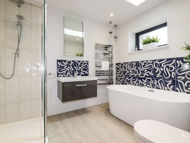 A bathroom with a shower cabin a floating sink cabinet a freestanding bathtub patterned tiles and a window with plants at Trenant View in Wadebridge
