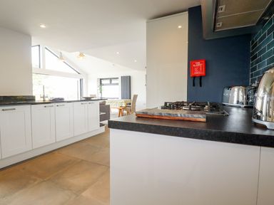 A kitchen with white cabinets a black countertop a gas stove toaster kettle and a dining area in the background at Trenant View in Wadebridge
