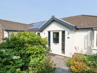 The front entrance of a single-story house with bushes and plants in front and solar panels on the roof at Trenant View in Wadebridge
