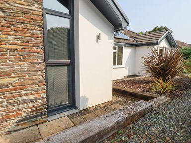 An exterior view of a building with stone and white walls gravel ground and plants at Trenant View in Wadebridge