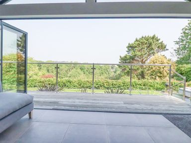 A room with tiled floor opening to a deck with metal railing overlooking trees at Trenant View in Wadebridge
