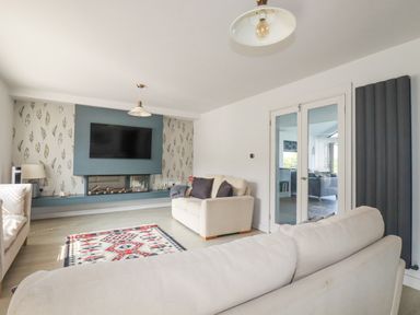 A living room with sofas a wall-mounted TV and glass doors at Trenant View in Wadebridge