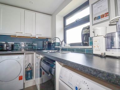 A kitchen counter with a sink washing machine microwave and various appliances at Trenant View in Wadebridge