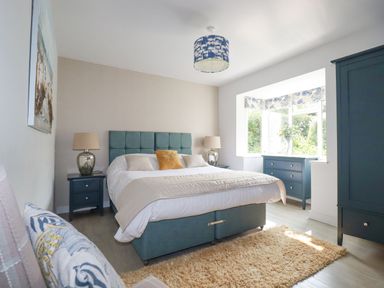 A bedroom with a double bed two bedside tables with lamps a window with a dresser and wardrobe at Trenant View in Wadebridge