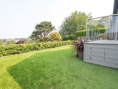 A garden with trimmed hedges trees and a glass railing deck at Trenant View in Wadebridge