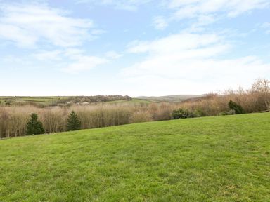 A grassy field with trees and rolling hills under a partly cloudy sky at Little May in Newquay