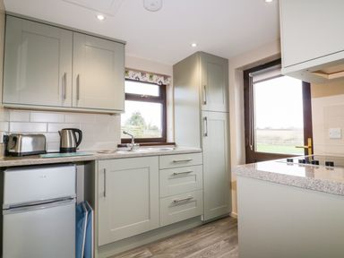 A kitchen with gray cabinets a small fridge a toaster kettle sink and stove with two windows and a door at Little May in Newquay