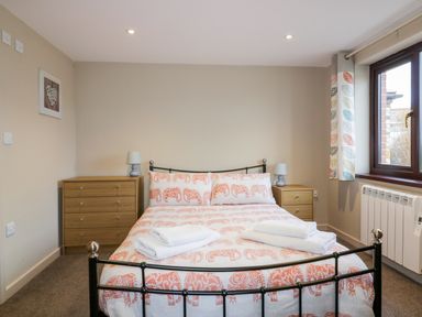 A bedroom with a double bed with orange patterned bedding two bedside tables with lamps a chest of drawers and a window with patterned curtains at Little May in Newquay