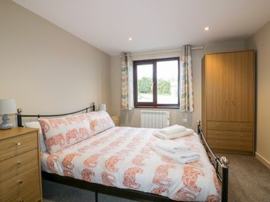 A bedroom with a bed with orange patterned bedding two wooden dressers and a window with patterned curtains at Little May in Newquay