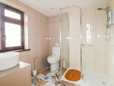 A bathroom with a toilet shower and sink with patterned floor tiles at Little May in Newquay