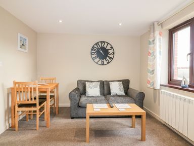 A living room with a grey sofa wooden coffee table dining table with chairs and a window at Little May in Newquay